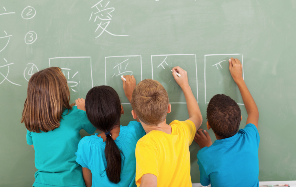 an image shows 4 kids write in Chinese in front of a blackboard